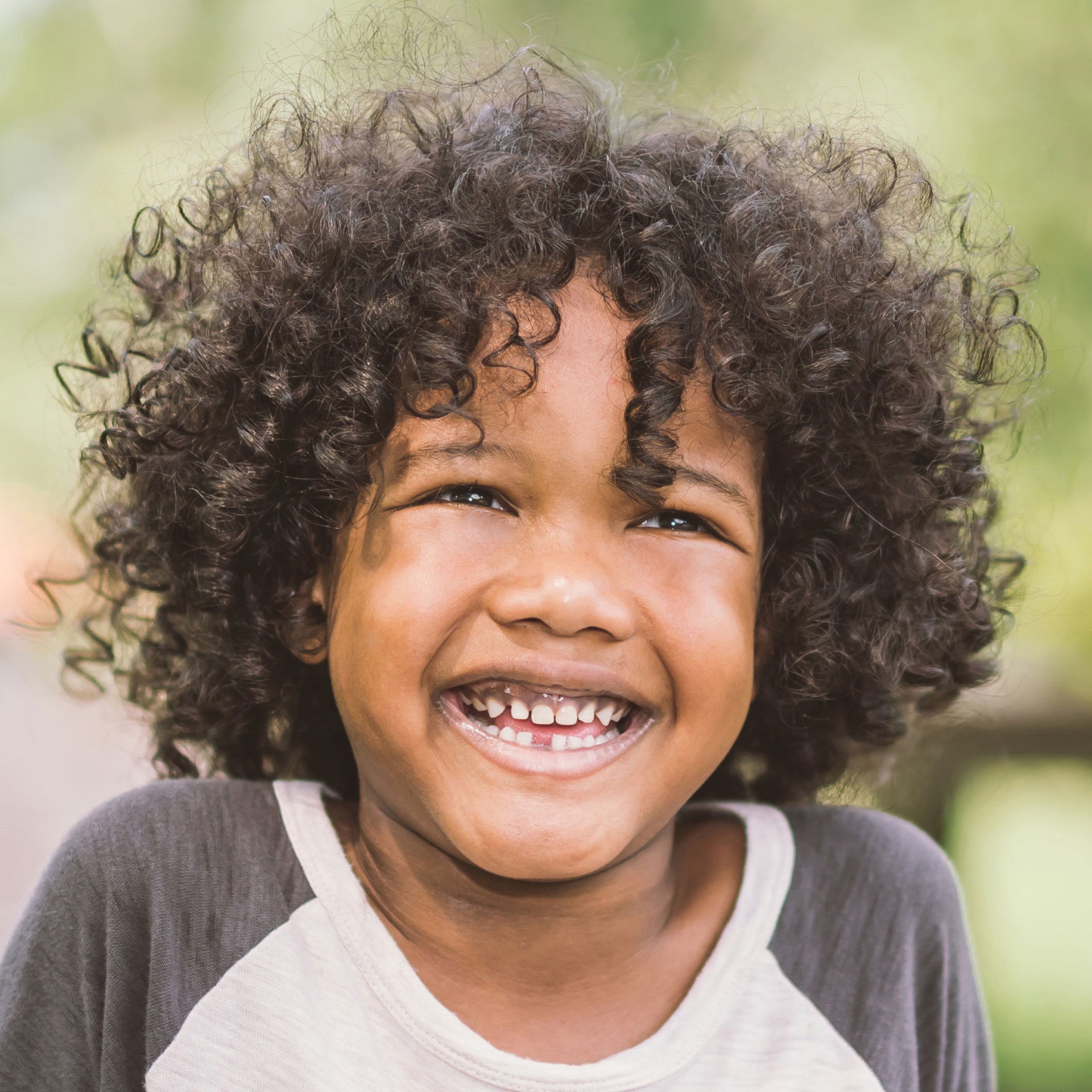 african american boy with curly hair missing a tooth and smiling while playing outside