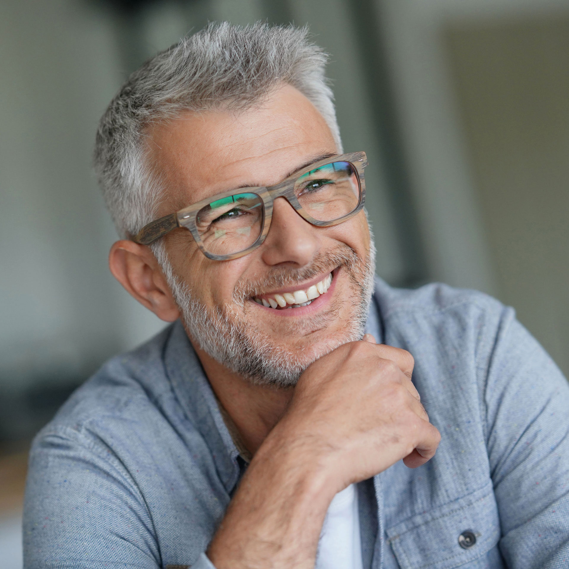 middle aged man wearing glasses resting his chin on hand looking to the right and smiling